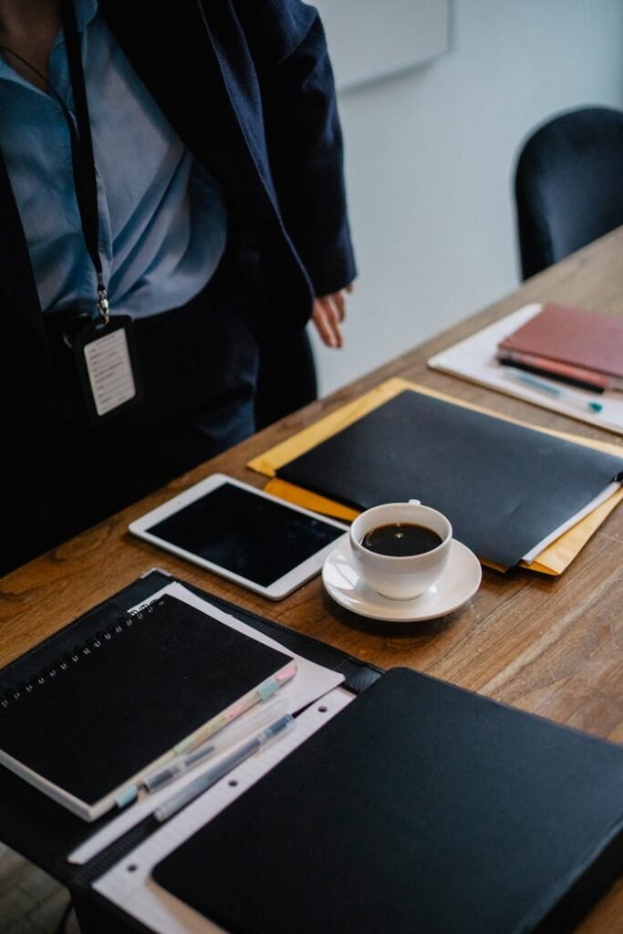 Crop anonymous businessperson in elegant outfit standing near wooden table with important document and cup of hot coffee in office